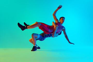 Fototapeta na wymiar Two men, athletes competing in a wrestling match, demonstrating skills and motivation to win against blue background in neon light. Concept of combat sport, martial arts, competition, tournament