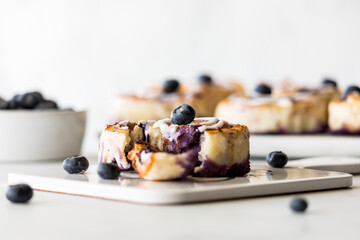 A homemade fresh blueberry cinnamon roll with more rolls in soft focus in behind
