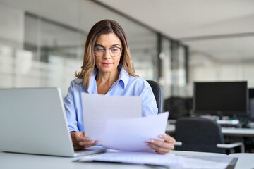 Busy mature business woman entrepreneur working in office checking legal document account invoice in office. Businesswoman of middle age manager executive or lawyer using laptop computer at work.