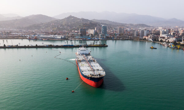 Aerial view of tanker ship in clear turquoise waters near coastal cityscape.