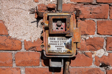 Old fire alarm button on a brick wall.  Inscription in Russian In case of fire, break the glass Press the button - obrazy, fototapety, plakaty