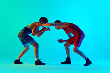 Wrestlers in action, young men in blue and red uniform, athletes demonstrating technique in their moves against blue background in neon. Concept of combat sport, martial arts, competition, tournament