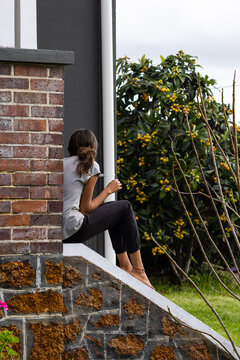 young girl turned away from camera sitting on steps of old house