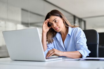 Obraz premium Worried fatigued mature business woman having headache at work. Tired upset busy 40s middle aged businesswoman feeling stress having problem at workplace looking at laptop computer in office.
