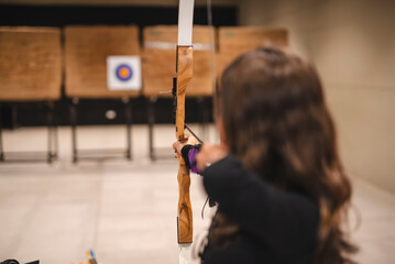 An Asian woman in her young adults practicing archery at an indoor range in a mall, aiming towards...