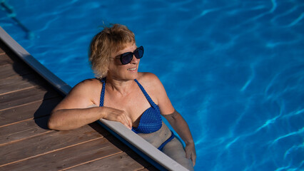 An elderly woman in sunglasses swims in the pool. Vacation in retirement. 