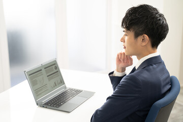 ノートパソコンで資料作成時に悩む男性ビジネスマン