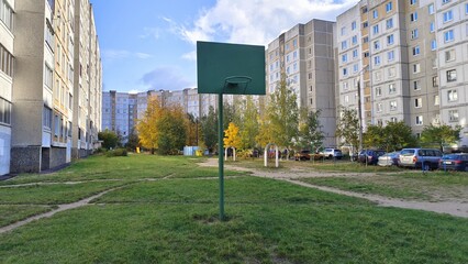 On the grass lawn is a metal pole with a basketball backboard and ring. Nearby are residential...