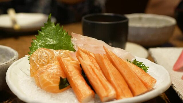 close up to a bowl of sashimi fresh raw fish japanese food while using chopsticks to pick salmon sashimi from bowl on ice to eat