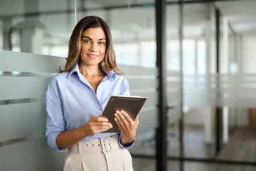 Poster Smiling mature business woman executive, happy middle aged businesswoman entrepreneur, 40 years old company hr holding digital tablet looking at camera standing in office at work. Portrait. © insta_photos