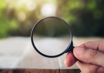 Hand holding magnifying glass on natural background. man looking through magnifying glass,...