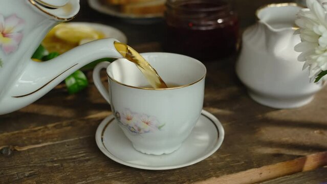 Pouring black tea from teapot into porcelain cup.