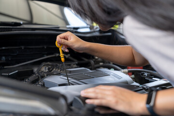 The woman is checking the engine oil of the car