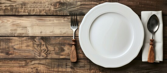 A white, vacant plate accompanied by utensils, set against a backdrop of wooden texture. - obrazy, fototapety, plakaty