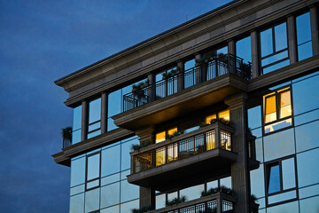 Apartment building, architecture facade at night. Modern apartment building facade in the city, light burns in one window of modern building with glass facade. Windows and balconies