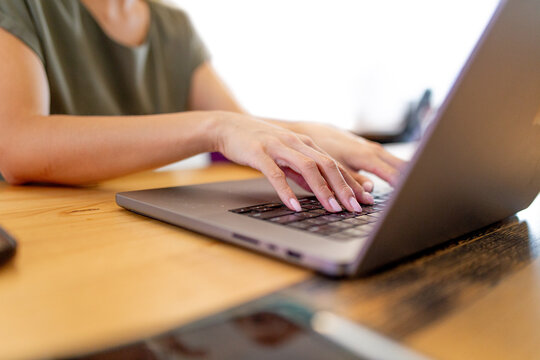 Close-up of woman's hands with her fingers on the keyboard of a laptop in an office