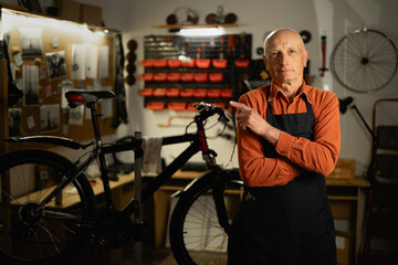 Happy man old man pointing with finger at space for text while working in garage or bicycle repair shop