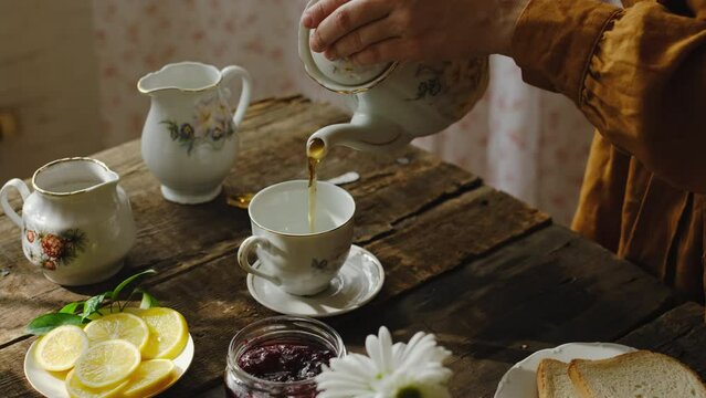 Tea party in rustic style. Pouring tea from teapot into porcelain cup.