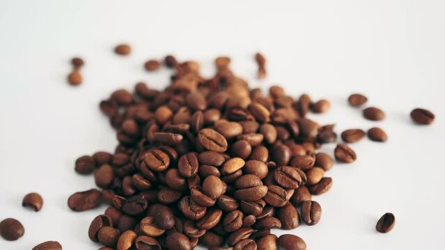 Brown coffee beans spill onto white table isolated background, close up. Aromatic bitter caffeine.