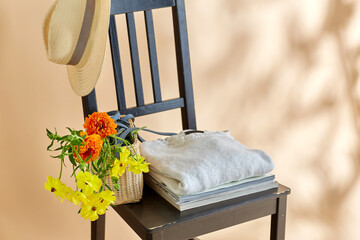 home decor and design concept - flowers in basket, clothes, hat and magazines on vintage chair over beige background