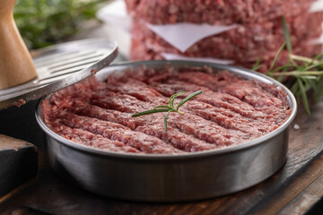 Fresh raw ground beef patties with rosemary salt and pepper made in a meat form on a cutting board - 789410900