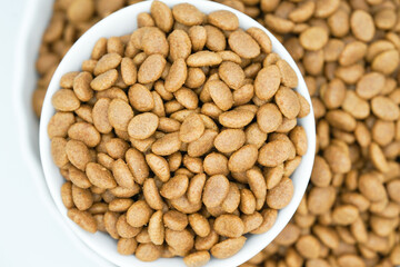Top view of dry pet food in a white bowl, dog and cat food background.