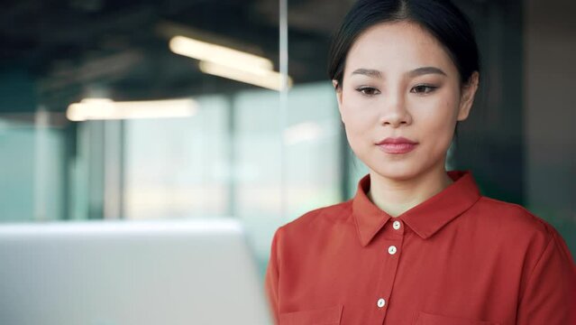 Happy asian female employee typing on laptop sitting at workplace in business office. Woman worker working in computer application, banking, texting, chatting online, busy with a project. Close up