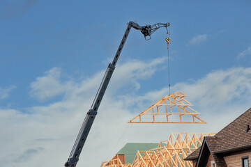 A crane lifting  a pre-fab roof truss onto a residential construction project