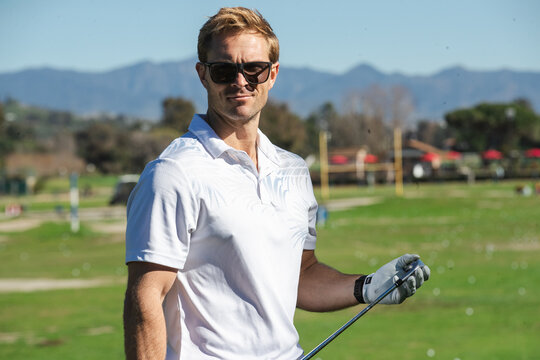 Handsome golfer on the driving range. The man is wearing sunglasses outside.