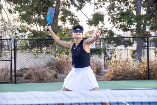 Female pickleball player hitting the ball during a game on an outdoor court. The Asian woman is a fit athlete playing the popular sport. 
