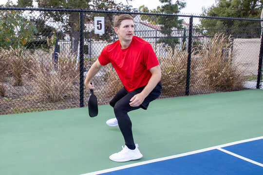 Skilled pickleball player on an outdoor court. The man is hitting the pickleball with his racquet over a net. 