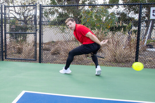 Skilled pickleball player on an outdoor court. The man is hitting the pickleball with his racquet over a net. 