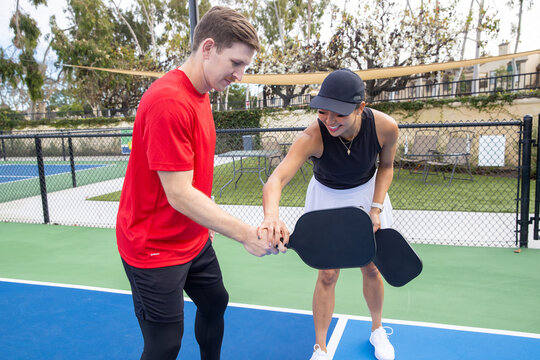 Female pickleball coach teaches her male student how to be a better player through practice and technique. The teacher is showing him how to hold his paddle properly. 