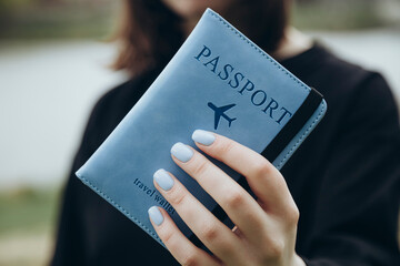 A passport in a blue cover in the hands of a woman with a blue manicure.