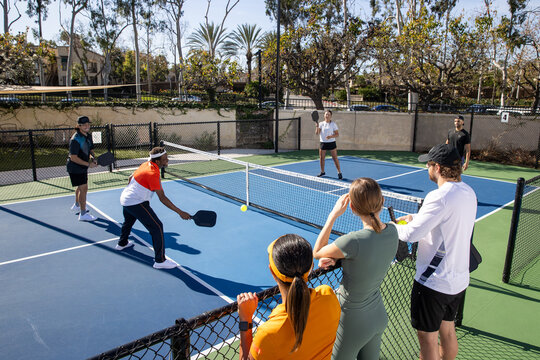 Pickleball players on an outdoor court playing the popular game. The sport is similar to tennis and allows for a diverse range of people to play. 