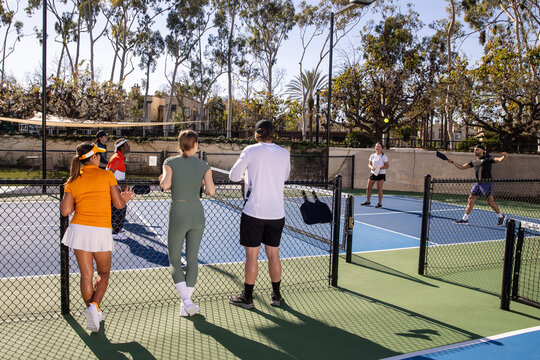 Pickleball players on an outdoor court playing the popular game. The sport is similar to tennis and allows for a diverse range of people to play. 