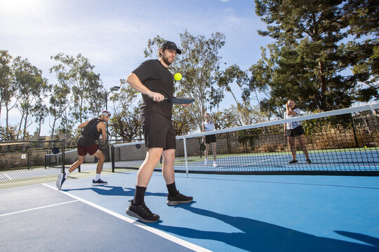 Pickleball players on an outdoor court playing the popular game. The sport is similar to tennis and allows for a diverse range of people to play. 