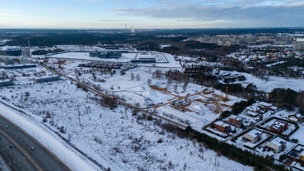Drone photography construction site covered by snow and heavy equipment working, surrounded by underdeveloped city suburb during winter day