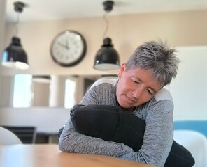 Woman with short gray hair, sitting, hugging a pillow with her head bowed on it, with a lost look....