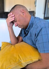 Adult man sitting on the sofa, with a pillow in his arms, desperate. Bad news. Economic problems. Poor health. Depression. Troubled divorce. Melancholic. Loss of a loved one