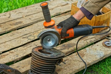 grinding orange electric dangerous powerful industrial machine in the hand and gloves of a worker cleans part of an iron engine from rust during the day on the street