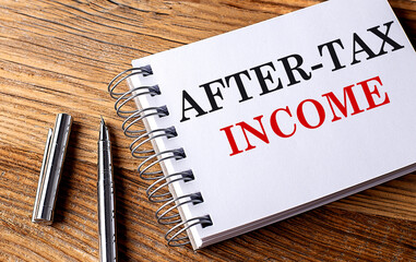 AFTER-TAX INCOME text on notebook with pen on the wooden background