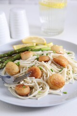 Delicious scallop pasta with asparagus, green onion and lemon served on white table, closeup