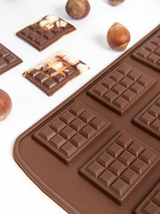 Silicone mold for chocolate on white background. Small chocolates and hazelnuts closeup. Vertical