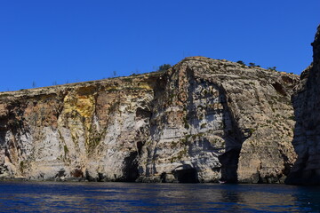 Fototapeta na wymiar ZURRIEQ, MALTA - Augusts 06, 2021: The Blue Grotto - A famous sea cave surrounded by the deep blue sea at southern Malta. On a traditional boat surrounded by more brightly coloured boats. 