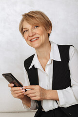 Portrait of business woman. Confident mature woman using mobile phone and typing on light gray background. Looking at camera. High quality photo