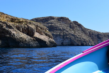 ZURRIEQ, MALTA - Augusts 06, 2021: The Blue Grotto - A famous sea cave surrounded by the deep blue sea at southern Malta. On a traditional boat surrounded by more brightly coloured boats. 