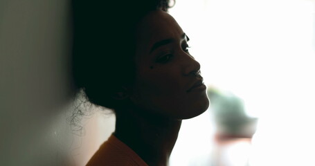 One depressed young black latina woman leaning on wall with melancolic expression gazing at distance feeling lost in thought, profile close-up face in silhouette