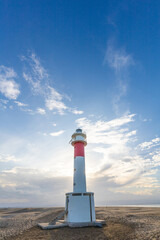 A lighthouse stands tall on a beach, with a clear blue sky above it