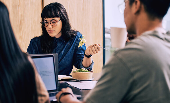 Business woman, computer and eating while working in a coworking office in a break room. Startup, salad and professional with web design project and internet research with lunch at company with food